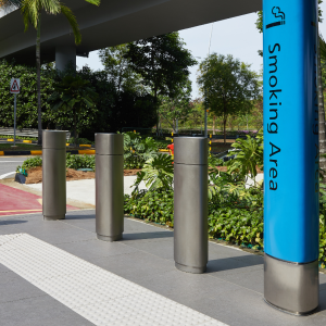 Row of stainless steel bollards with aesthetic sleeves. One of which has a 'smoking area' sign wrapped around it.